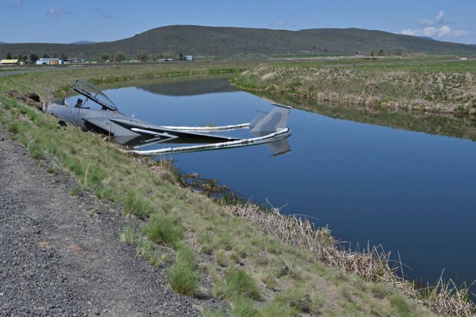 Un F-15D de la Fuerza Aérea de EE.UU. asignado al Ala de Caza 173 se encuentra en un canal del Bureau of Reclamation en el lado sur de la pista tras un aterrizaje forzoso en Kingsley Field en Klamath Falls, Oregón, el 15 de mayo de 2023. Barreras absorbentes rodean la aeronave como precaución contra la fuga de combustible u otras sustancias. (Foto de la Guardia Nacional Aérea de EE.UU. por el sargento mayor Jefferson Thompson)