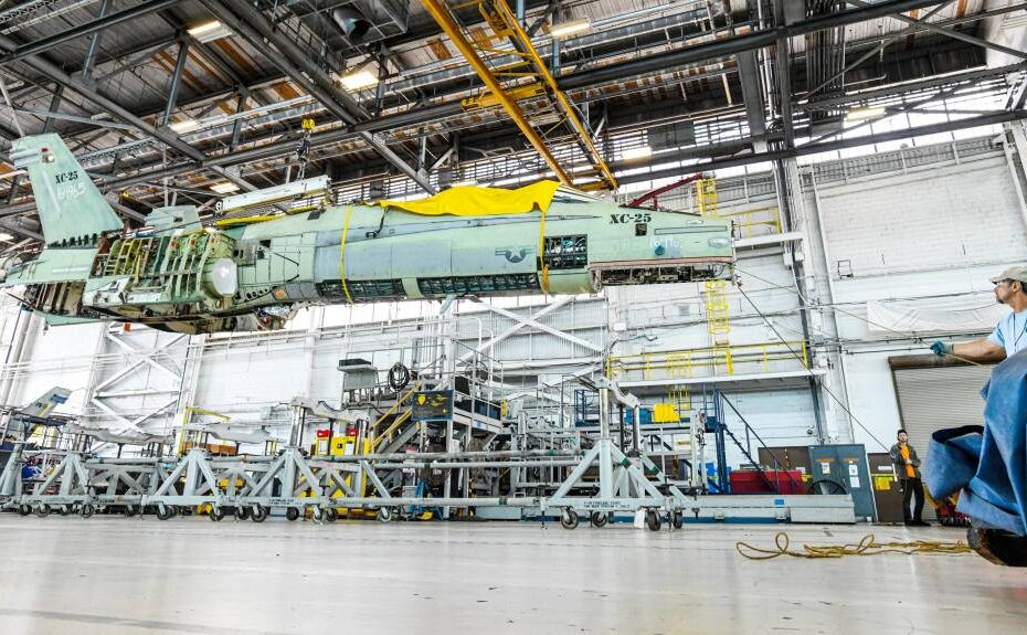 Un miembro de la tripulación del Fleet Readiness Center Southeast (FRCSE) ayuda a estabilizar un F/A-18 Hornet mientras se reposiciona utilizando una grúa como parte de la evolución del mantenimiento del Center Barrel Replacement (CBR). Los CBR se llevaron a cabo para prolongar la vida útil de los aviones F-18A-D, ahorrando al gobierno de EE.UU. millones en costes de sustitución. (Foto de la Marina de los EE.UU. por Toiete Jackson)