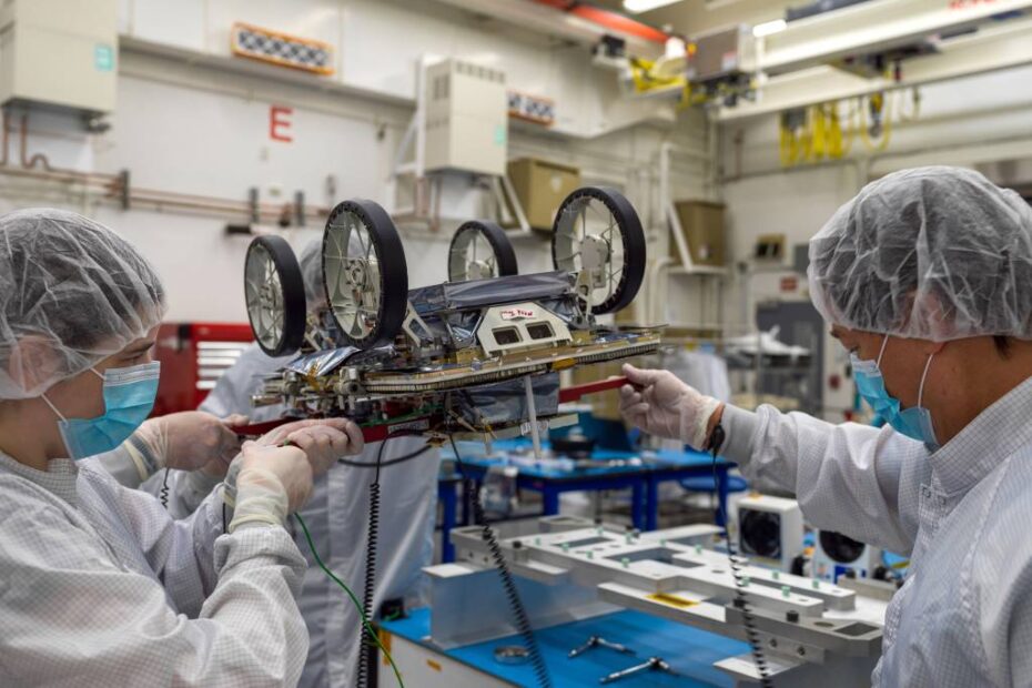 Miembros de un equipo del JPL que trabaja en la demostración tecnológica CADRE de la NASA utilizan asas rojas temporales para mover uno de los pequeños vehículos lunares del proyecto y prepararlo para su transporte a las instalaciones de Intuitive Machines en Houston, donde se acoplará al tercer módulo de aterrizaje lunar de la empresa. Crédito: NASA/JPL-Caltech