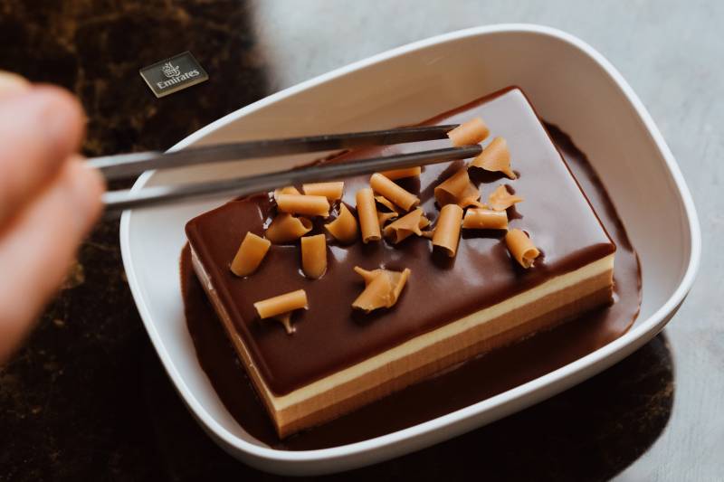 La imagen muestra un postre de la clase económica de Emirates a base de chocolate: el pastel de mousse de triple chocolate de Emirates con salsa de chocolate y virutas de caramelo. ©Emirates