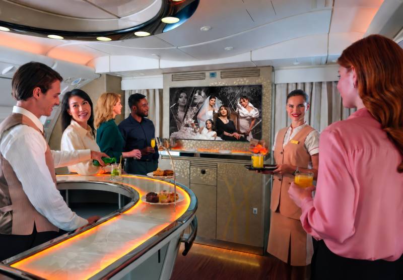 La imagen muestra a pasajeros de Emirates disfrutando de «Dubai+» en el salón de a bordo de primera clase y clase ejecutiva: una selección exclusiva de contenido de entretenimiento de los Emiratos y de la región, disponible a través del galardonado sistema de entretenimiento a bordo «ice» de la aerolínea. ©Emirates